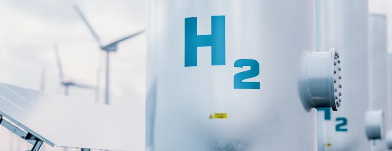 Hydrogen energy storage gas tank with solar panels and wind turbine in background.